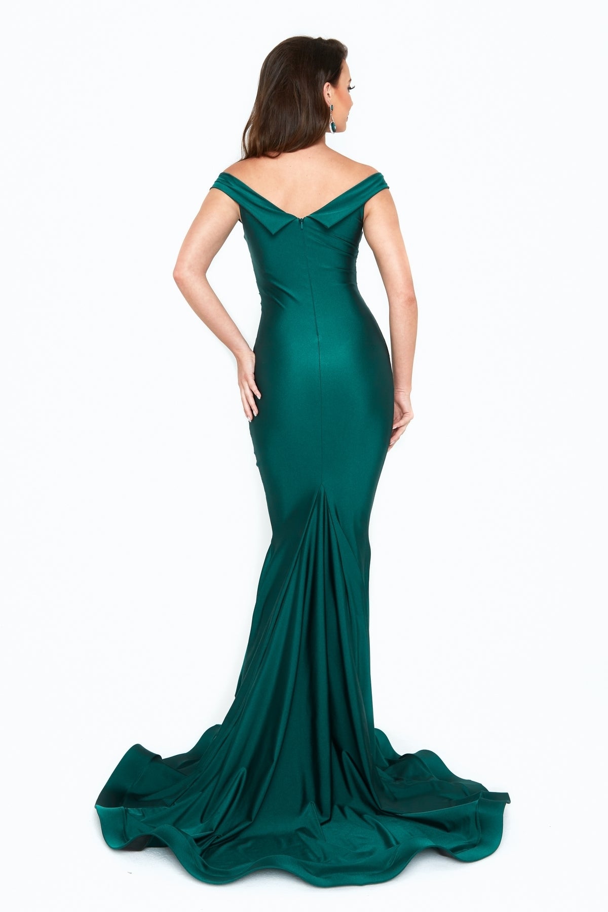 Woman in a fitted, floor-length Criss-Cross Long Mermaid Prom Dress (Atria 6519H) in emerald green, standing against a white background and highlighting the gown’s elegant train from the back.